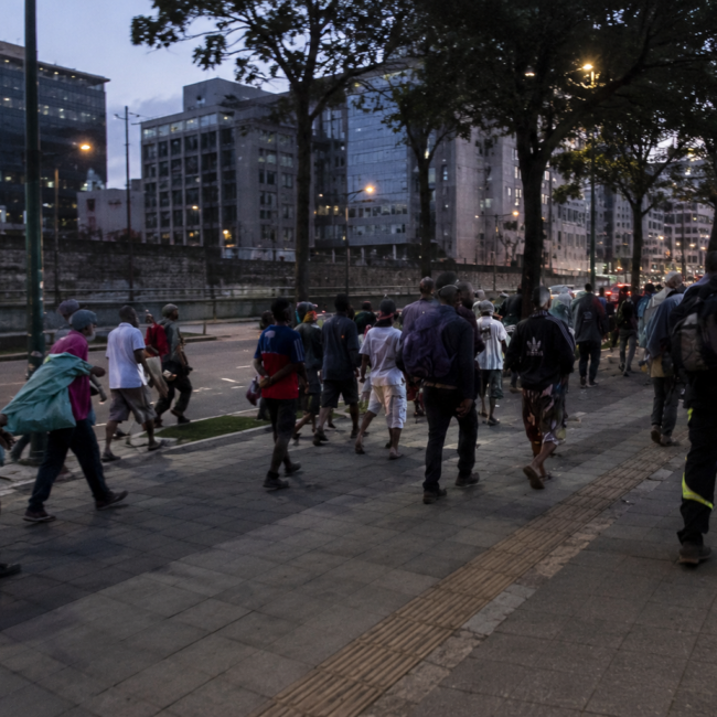 Grupo de pessoas em situação de vulnerabilidade caminhando por área urbana durante o entardecer, ilustrando os impactos das drogas sintéticas e da dependência química no Brasil.